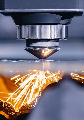Close-up photo of a plasma cutter as it cuts through a steel plate with sparks shooting down