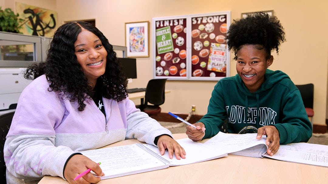 两个年轻的黑人女学生坐在一张桌子旁，打开笔记本一起学习