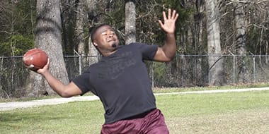 young black male leaning back to pass a football