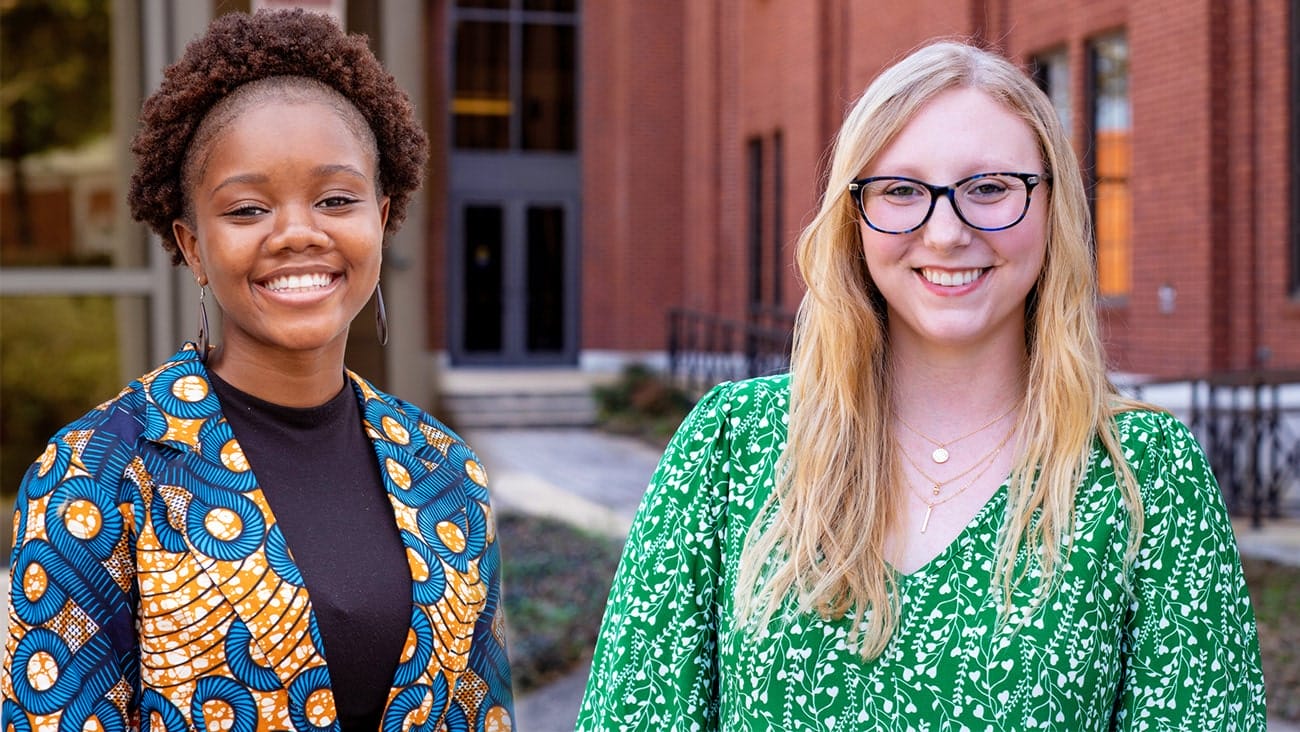 Portraits of a young black female and a young white female in front of brick building