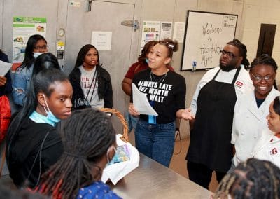 High school students gathered around a steel kitchen counter while learning about a culinary program