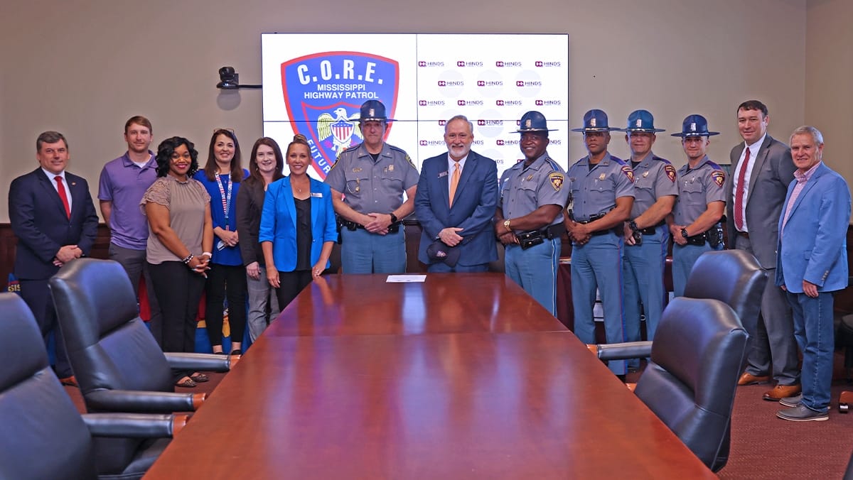 Posed group photo of college administrators and members of the Mississippi Highway Patrol standing around a long boardroom table
