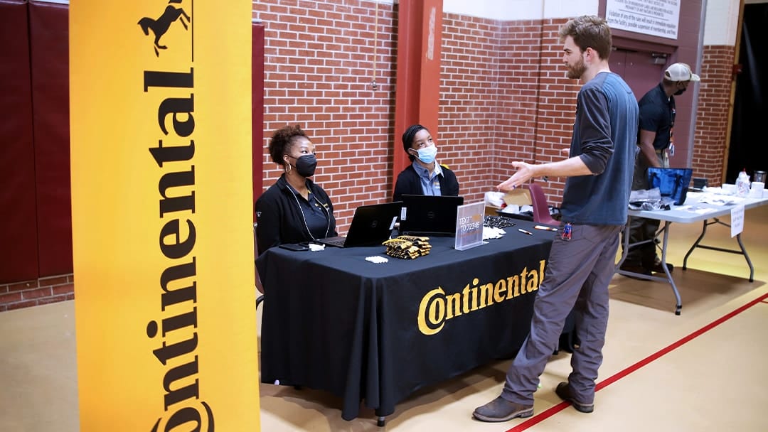 Two employees from Continental Tire speaking with a male student in a basketball gym
