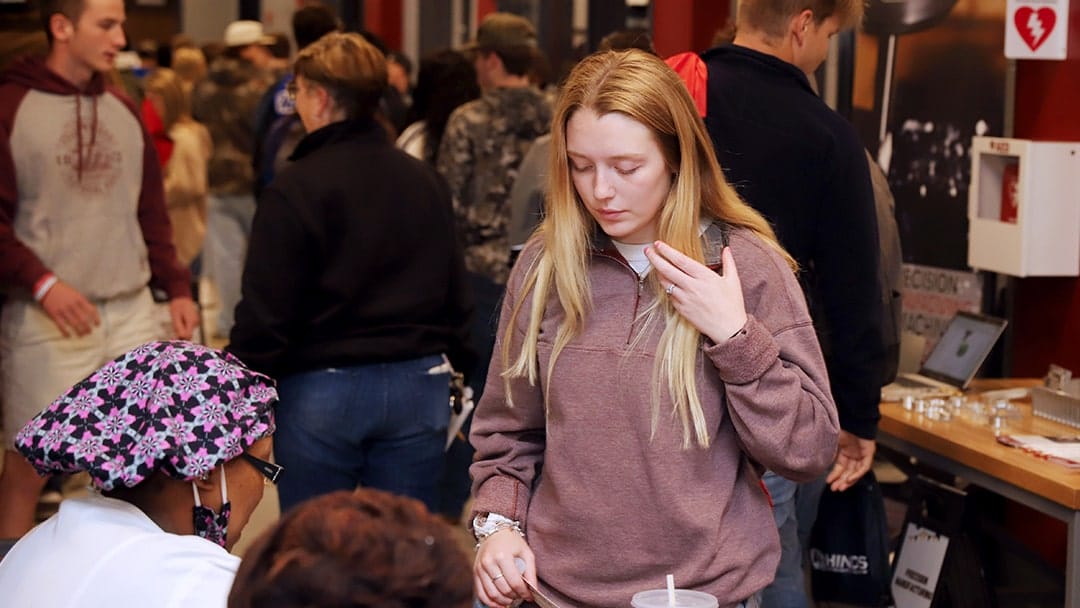 A blonde-haired female student waits to speak with college administrators in a crowded hallway