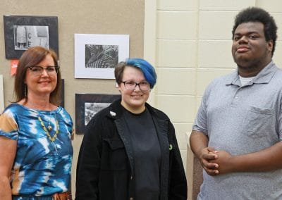 Three students standing in front of black and white photos on exhibit at college student art show