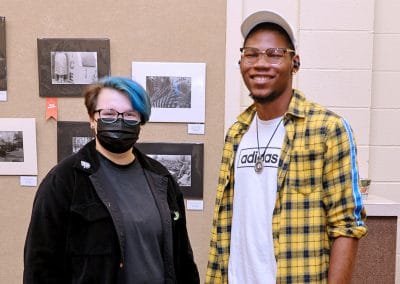 Two art students posing with black and white photos behind them