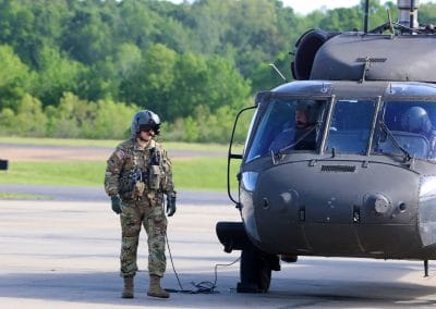 Pilot wearing camouflage fatigues walking around the front of the helicopter on the runway