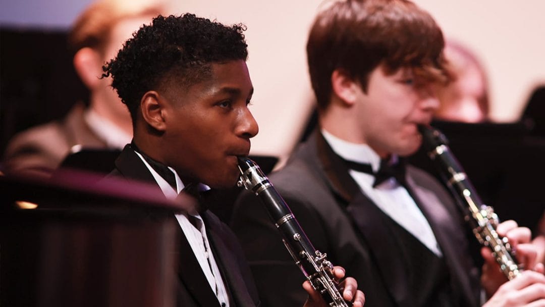 Two young male college students in tuxedos playing clarinets in a band concert