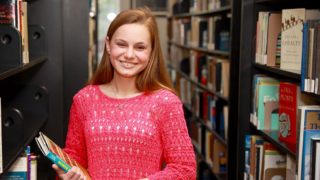 young white female student standing between library shelves